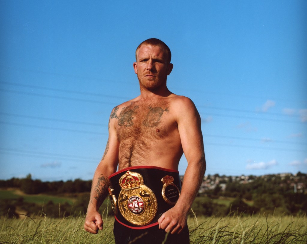 A fighter stands beneath blue skies with his winning belt