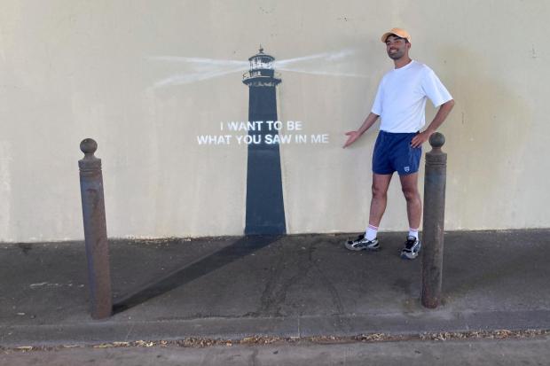 A man poses by an artwork by street artist Banksy