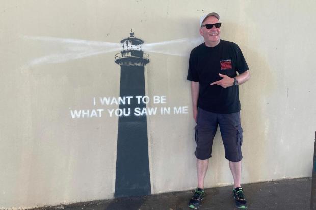 A man poses by an artwork by street artist Banksy