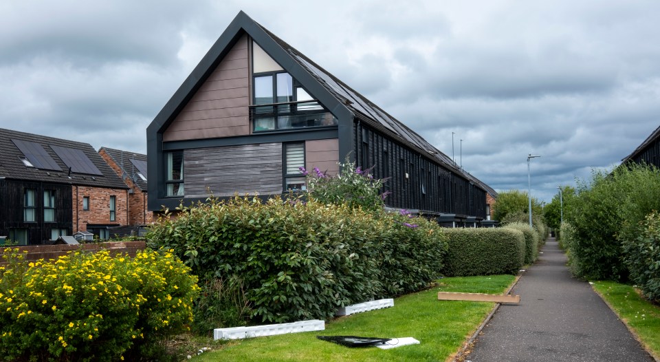 A discarded television and packaging lie on the grass outside a row of modern houses.