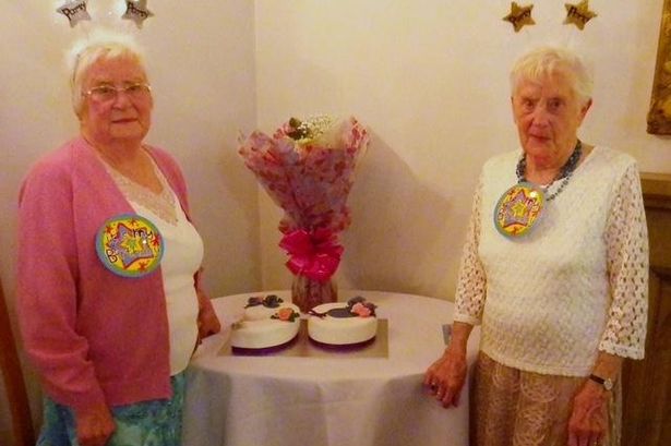 Two women with grey hair with birthday badges on 