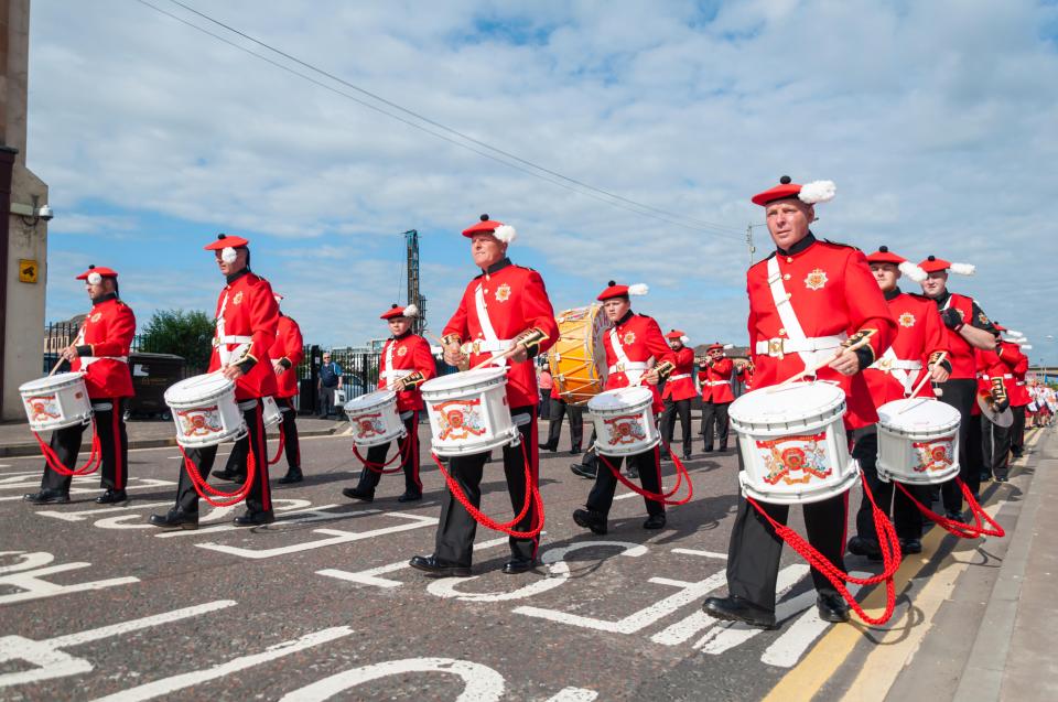 Marching band members in red uniforms playing drums in a parade.