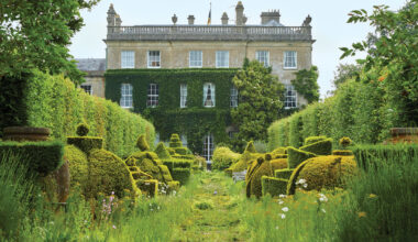 Manor house with lush green gardens, topiary forms, and a variety of flowers, creating a serene and picturesque scene.