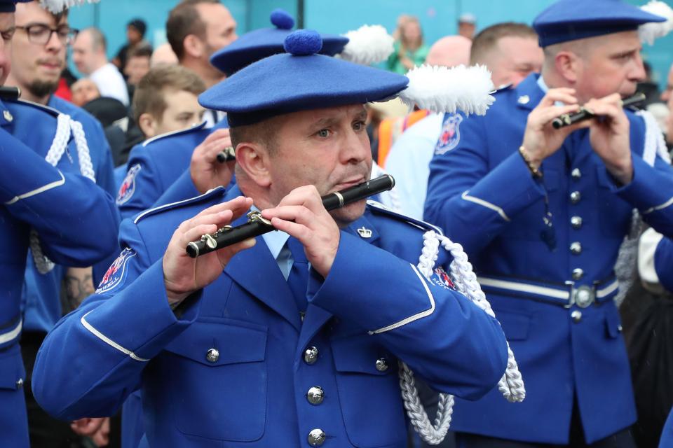 A man in a blue uniform plays a flute in a parade.