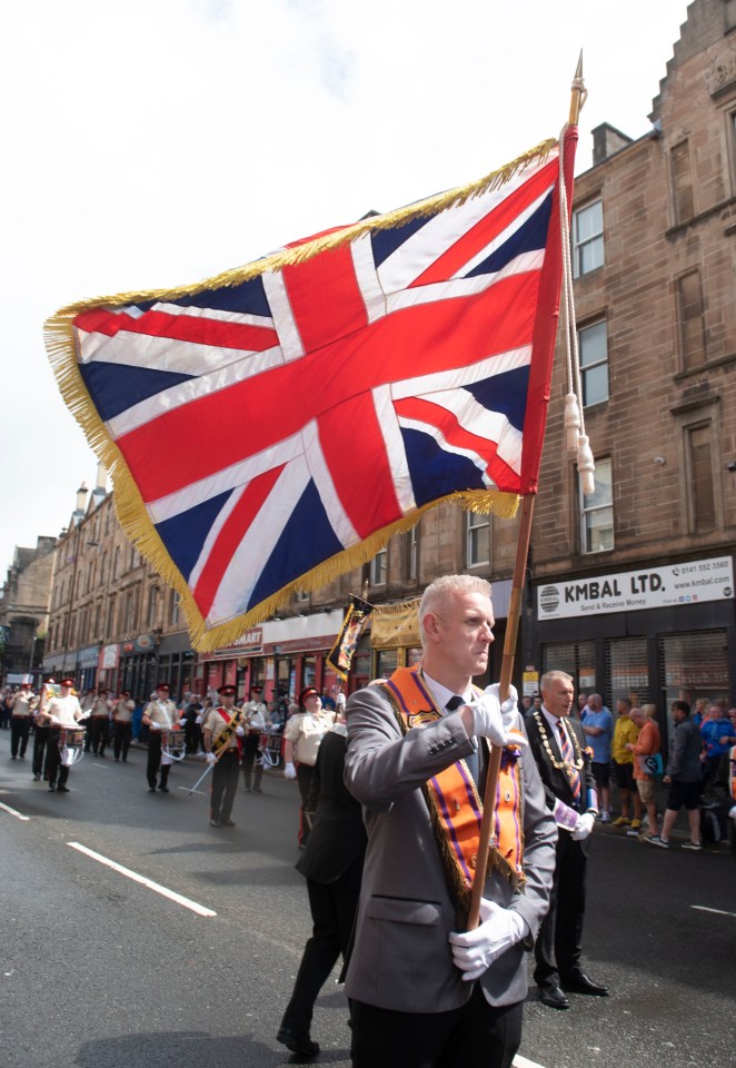 Man in a suit carrying a Union Jack flag in a parade.