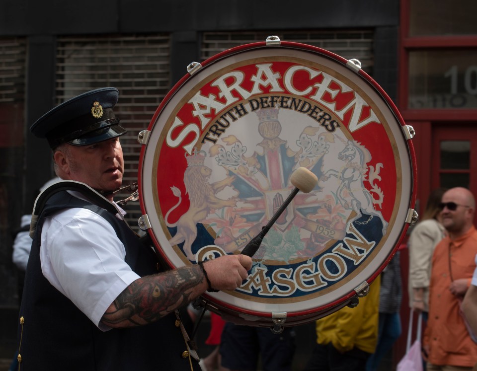 A man in a uniform plays a bass drum with the words "Saracen Truth Defenders Glasgow" on it.