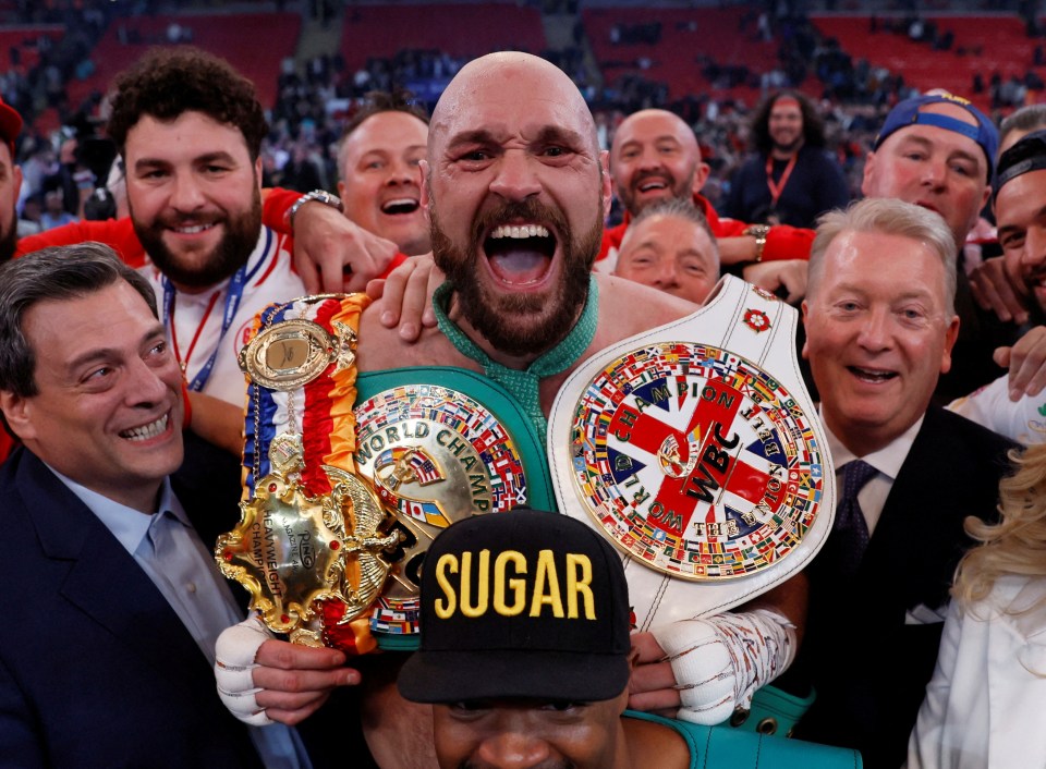 Tyson Fury celebrating a boxing victory with championship belts.