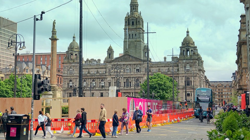 George Square in Glasgow, Scotland under renovation, with large advertising posters on the construction barriers.