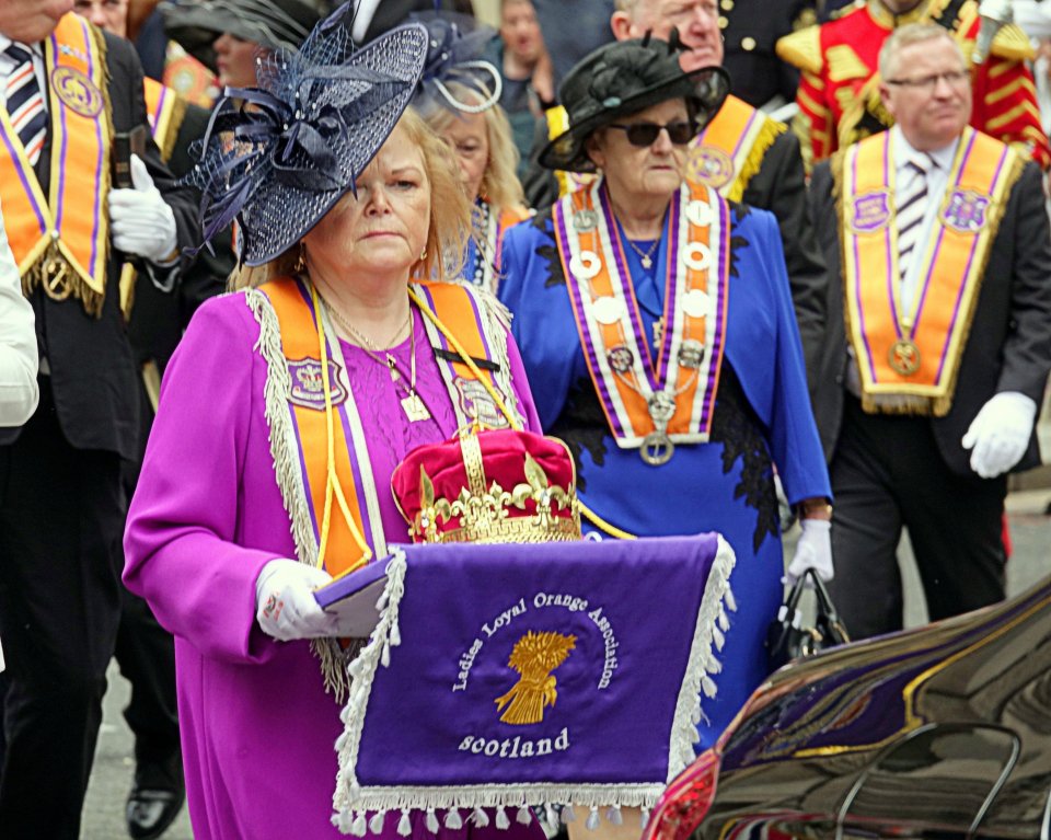 Woman in purple holding a crown and banner at an Orange Order parade.