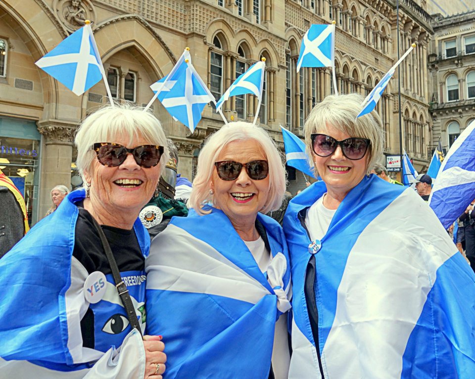 Three women at an independence march in Glasgow, Scotland, wrapped in Scottish flags.