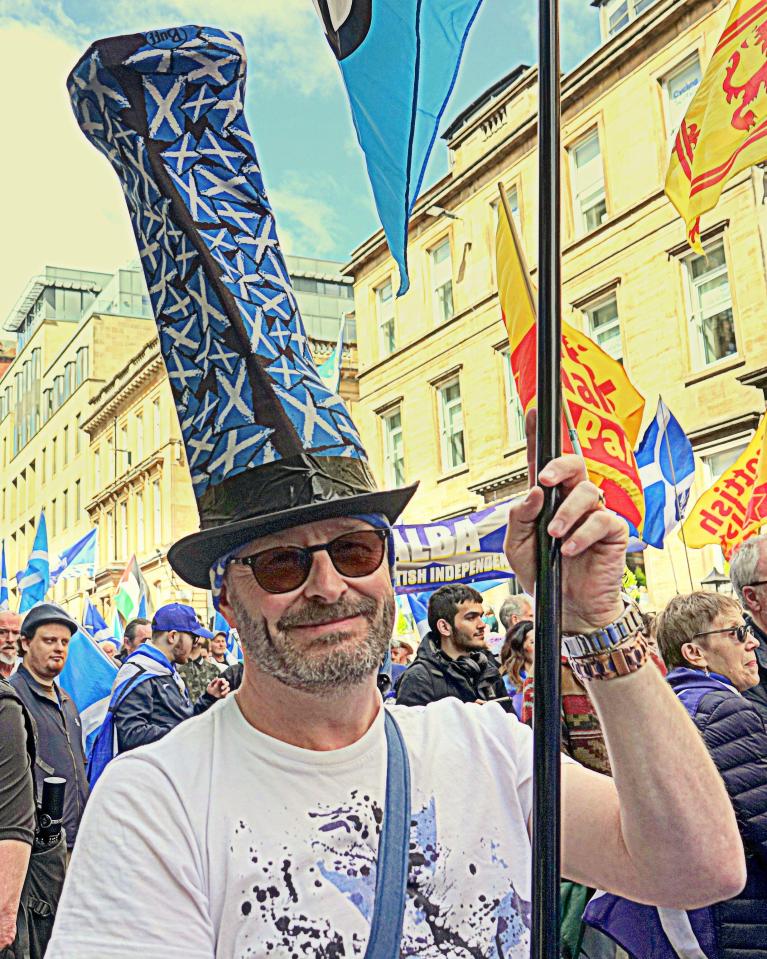 Man at Scottish independence march wearing a tall hat decorated with Saltires.