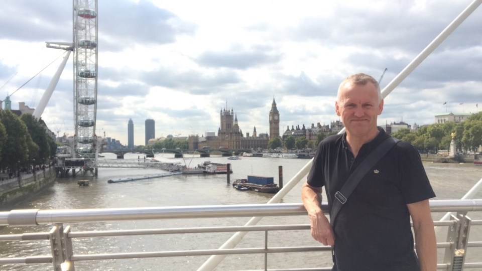 Man on a bridge in London, with the London Eye and Houses of Parliament in the background.