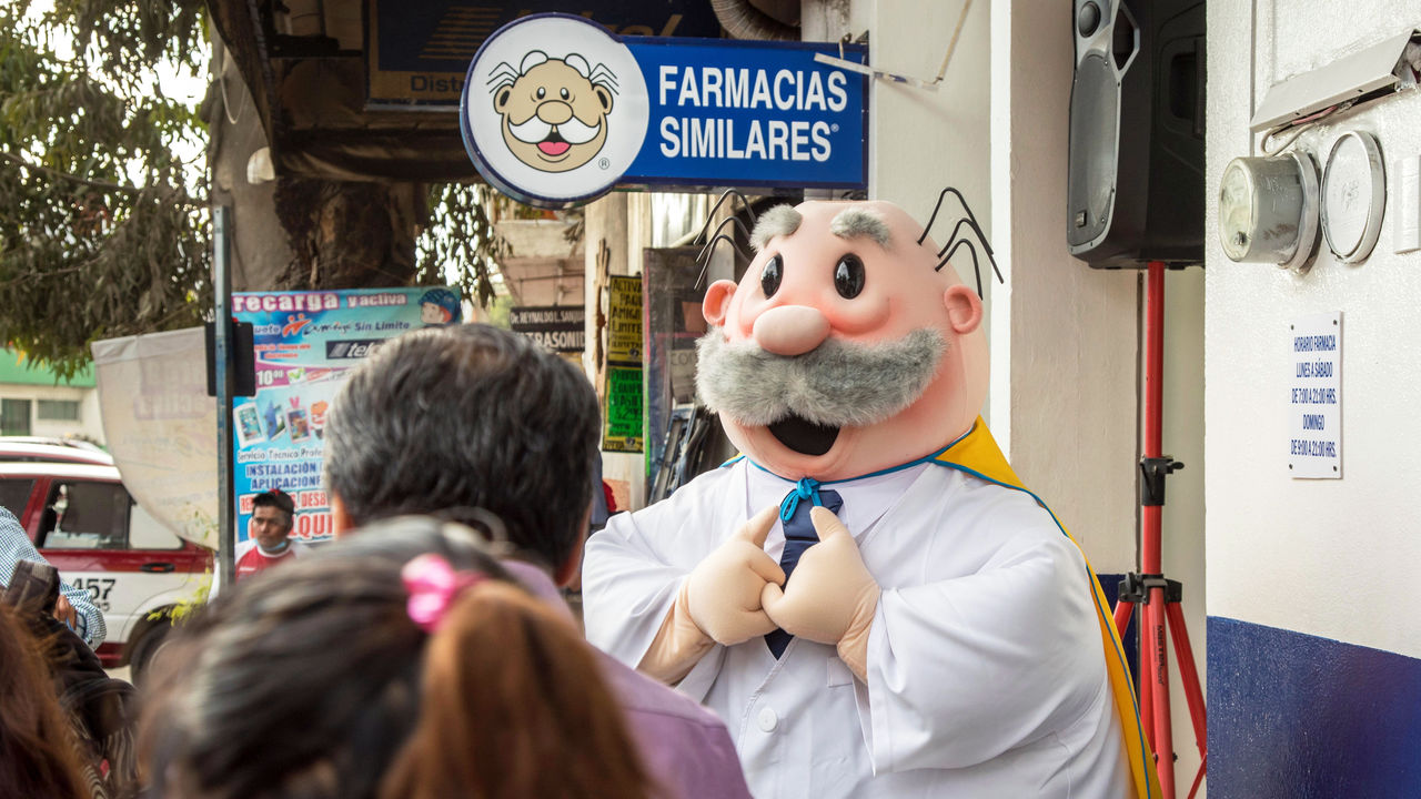 A person in a doctor costume solicits business for a Farmacias Similares store