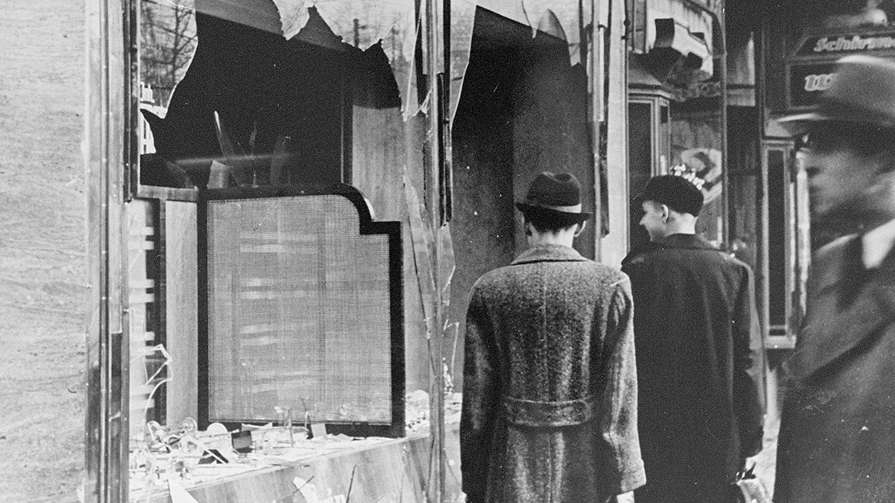 Germans pass by the smashed windows of a Jewish-owned shop after Kristallnacht