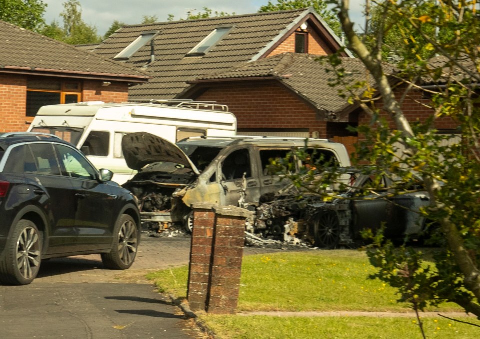 Two burnt-out cars in front of a house.