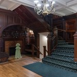 A wood paneled room with a fireplace, chandelier, and carpeted staircase.