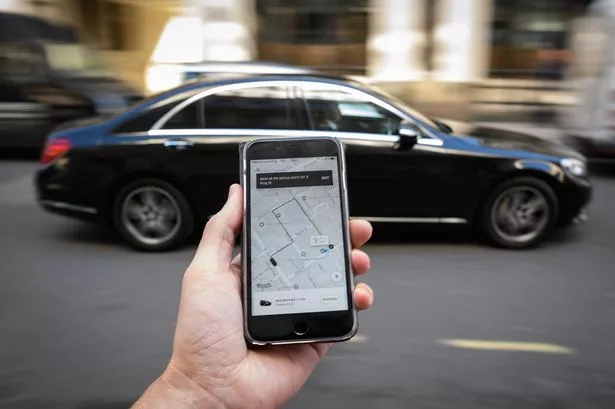 Man holding mobile phone with taxi route as car passes by on road