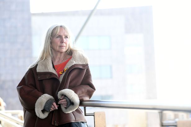 A blonde haired woman in a sheepskin coat looking across the camera