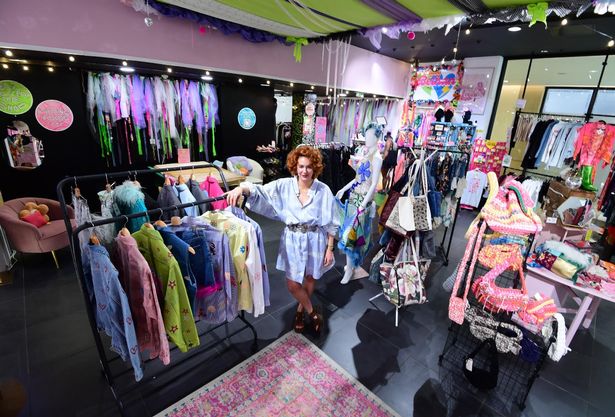 This photo shows a woman standing in a purple dress in a clothing and accessories shop. 