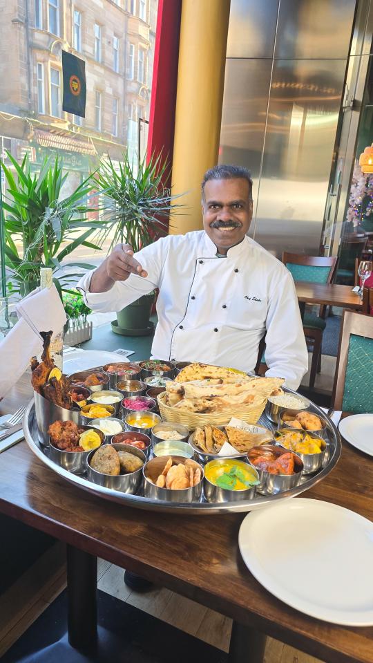 Chef pointing at a large platter of Indian food.