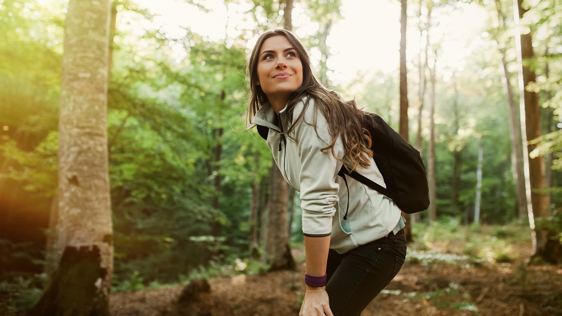 Woman in a forest wearing backpack and walking in nature smiling