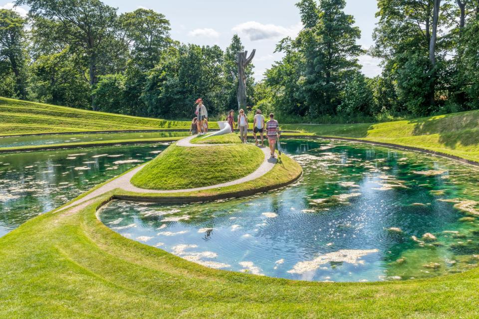 Visitors walking along a path by a pond at Jupiter Artland.