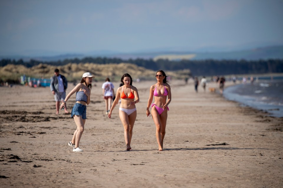 Three women walking on a sunny beach.
