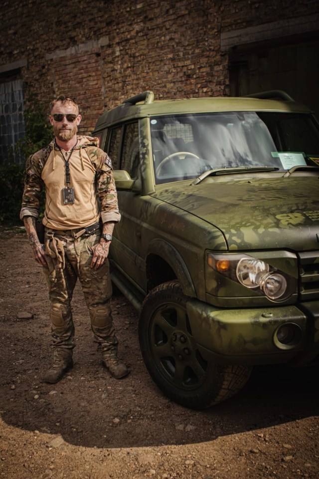 Man in camouflage standing next to a military vehicle.