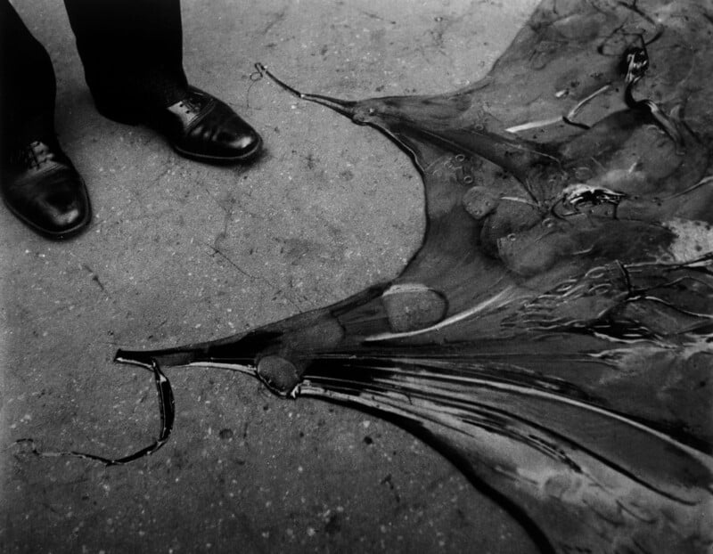 A pair of polished shoes stands on a concrete surface next to a broken, overturned umbrella, its metal ribs splayed and fabric drenched with water.