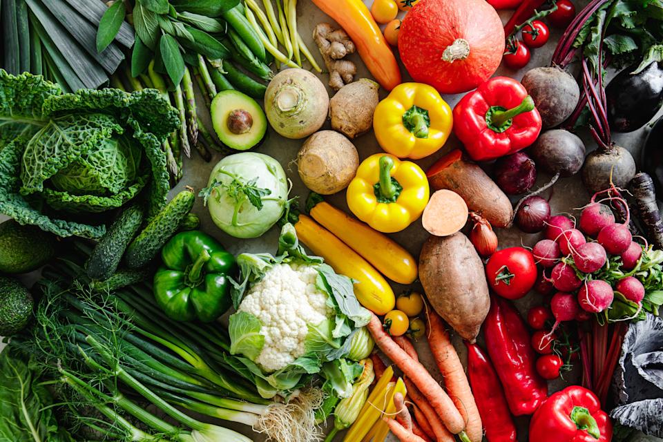A variety of fresh vegetables including cabbage, carrots, peppers, radishes, and more are laid out