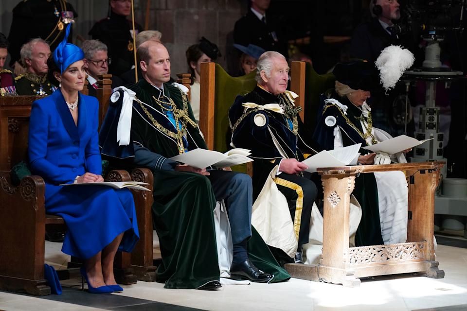 Kate Middleton wears a royal blue dress and matching hat, while Prince William and King Charles wear regal royal outfits