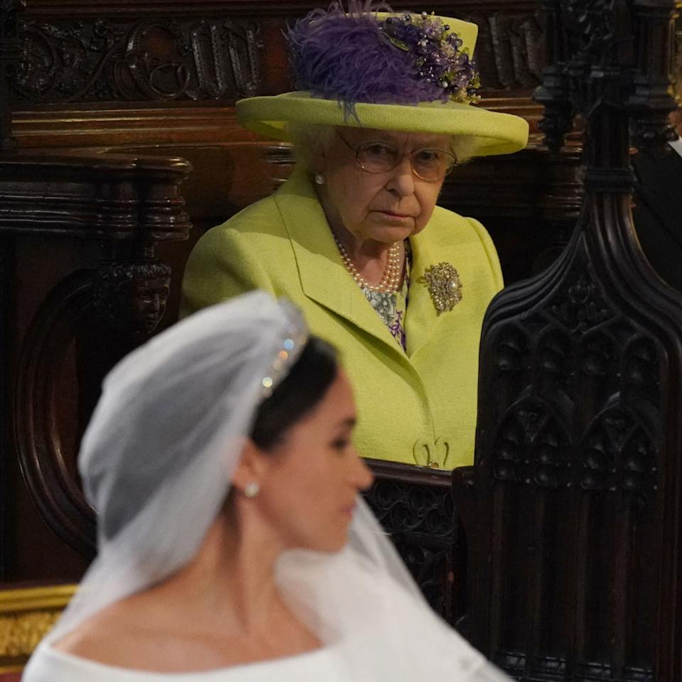  Queen Elizabeth wears a lime green outfit and looks at Meghan Markle who is wearing a veil and white wedding dress at her nuptials to Prince Harry on May 19, 2018. 