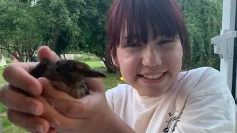 Family handout A young girl holding a small chick and smiling at the camera. She is wearing a white top and has fringe over her face.