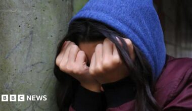 Unidentifiable young person wearing a blue hood with head in hands