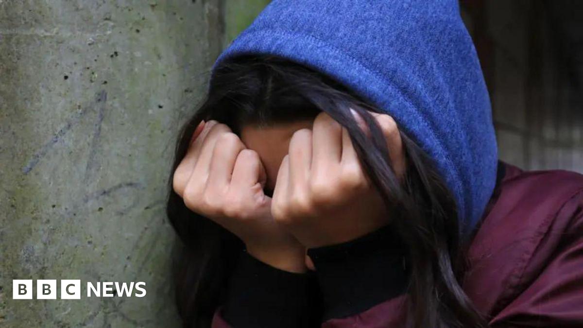 Unidentifiable young person wearing a blue hood with head in hands