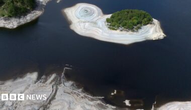 An aerial view of Haweswater reservoir, which shows receding water levels exposing light brown silt-beds.