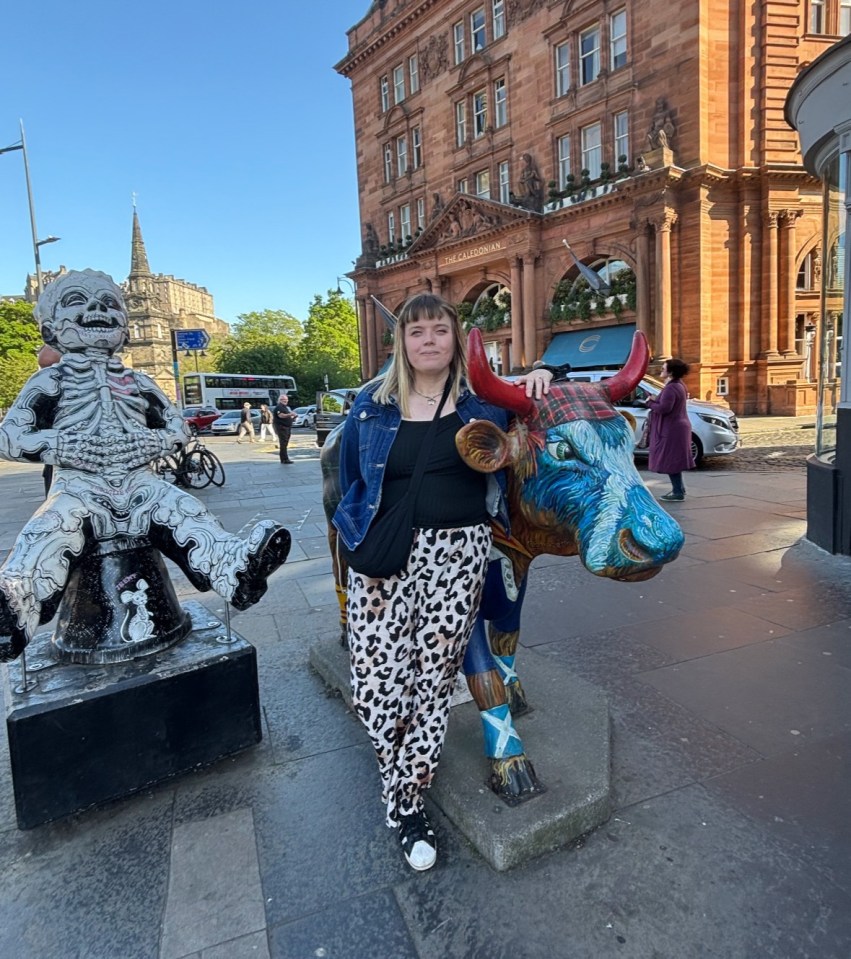 Woman posing with painted cow statue in front of building.