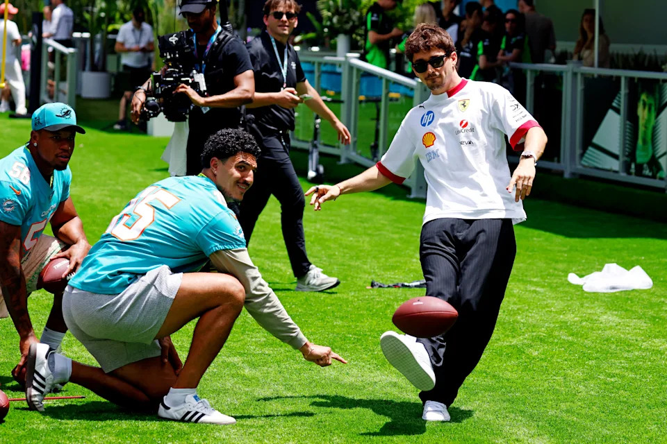 May 1, 2025; Miami Gardens, FL, USA; Ferrari driver Charles Leclerc (16) kicks mini field goals while Miami Dolphins player Jaelan Phillips holds the ball ahead of the F1 Miami Grand Prix at Miami International Autodrome. Mandatory Credit: Peter Casey-Imagn Images