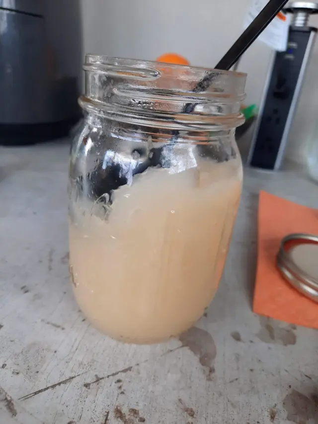 One jar of sea moss gel on a bench wit spoon wey stick out of di top.