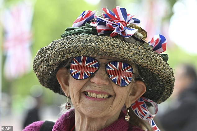 A woman wears British flag sunglasses earrings, hat and ribbons as she takes her place on the Mall