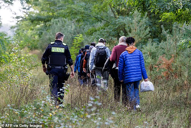 An officer of the German Federal Police (Bundespolizei) escorts a group of migrants near Forst, eastern Germany on October 11, 2023