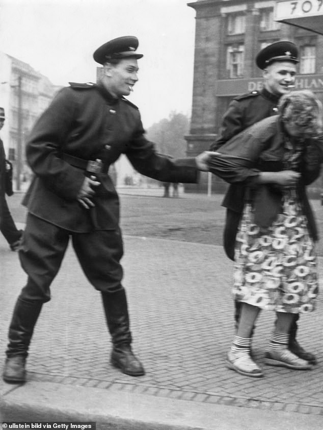 Two Russian Red Army soldiers grin with amusement as they grab at a girl in Leipzig, Germany during the postwar period