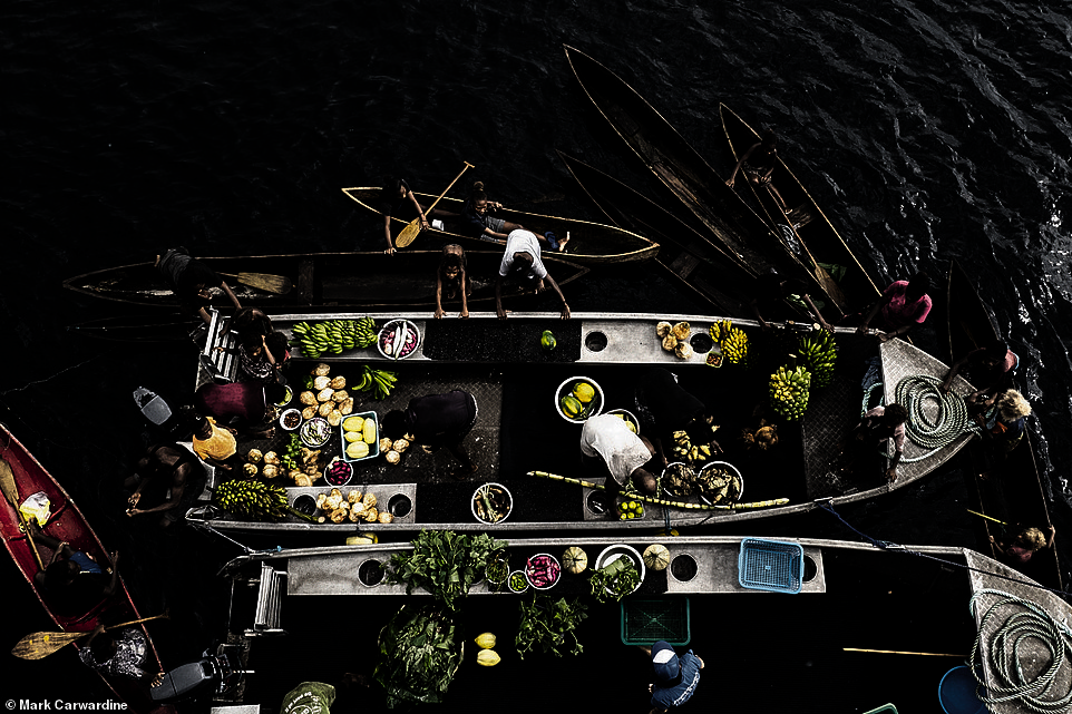 Solomon Islanders are photographed as they sell their 'fresh fruit and vegetables' from dugout canoes in this spellbinding image taken by Mark Carwardine