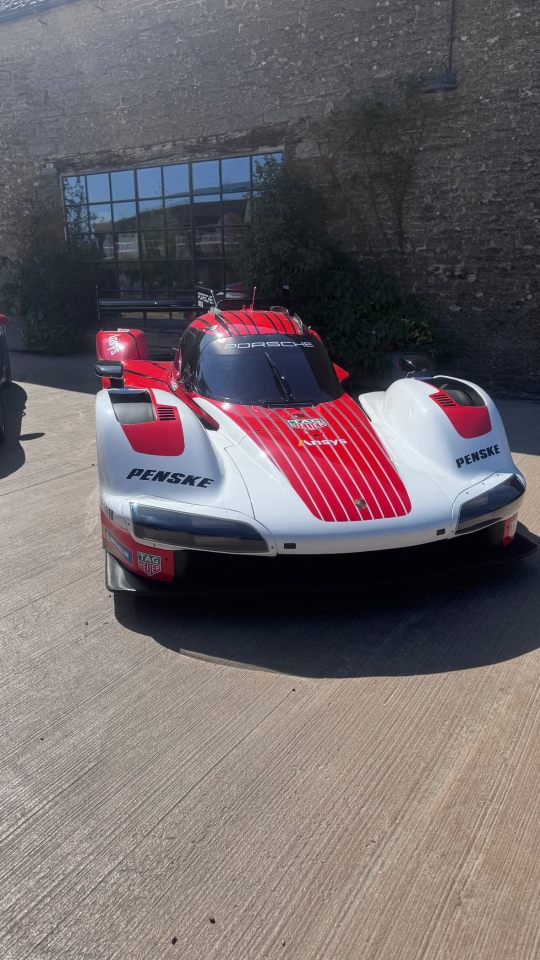 Red and white Porsche race car parked in front of a stone building.