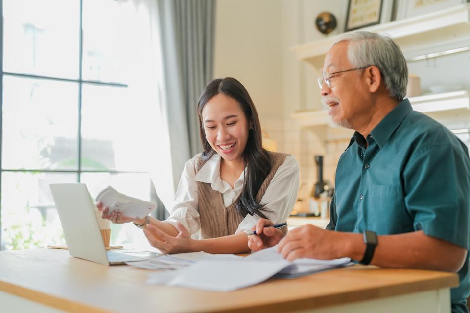A young woman and an older man smile while discussing documents at a table with a laptop