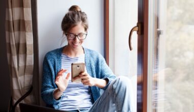 Holiday shopping online. Young woman makes purchases in the Internet. Freelancer pays by using smartphone on Black Friday. Happy girl is enjoying buying gifts and sitting by window with laptop at home