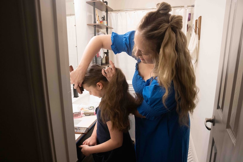Marley Mansour, 11, watches videos as her mom Kayla Mansour brushes her hair at their home...