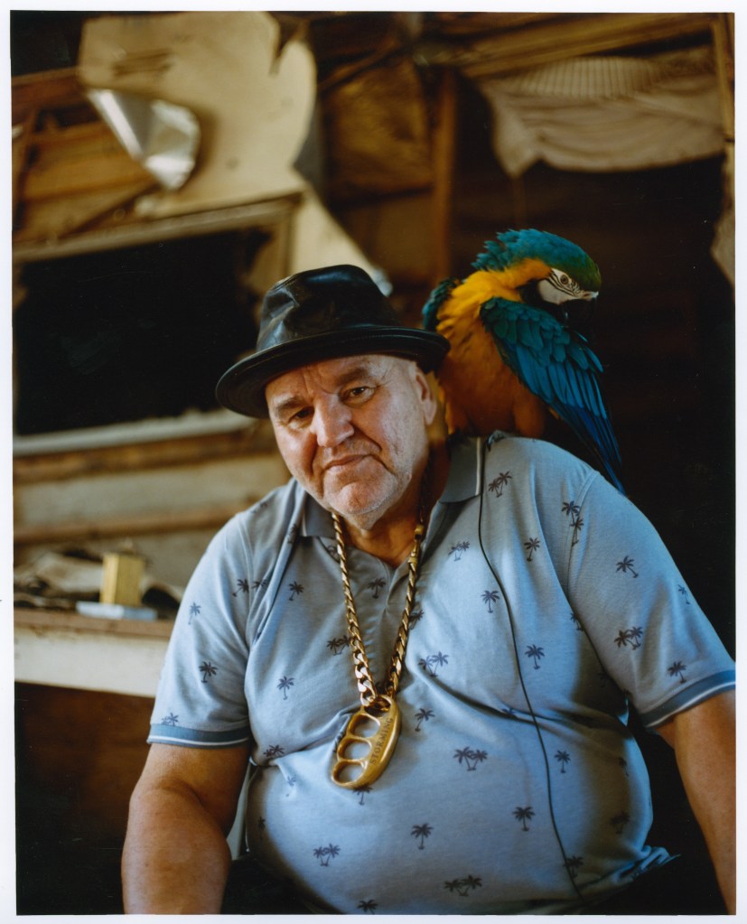 A man in a leather hat poses with a parrot