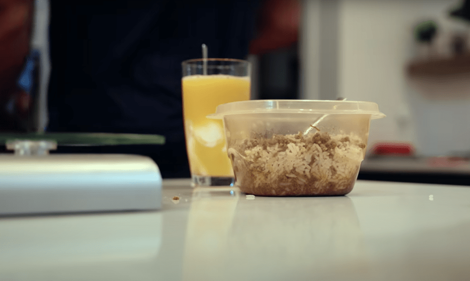 Rice and meat dish in a plastic container, next to a glass of orange juice.