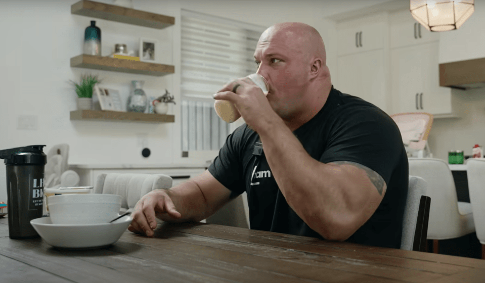 A large man sits at a table drinking from a cup.